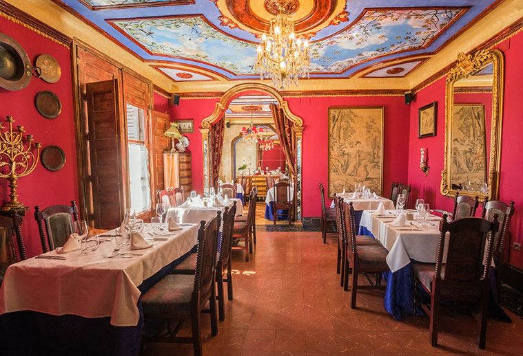Salón rojo con techo de frescos y mesas vestidas para banquete