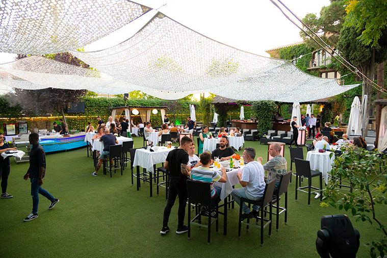 Comensales en la terraza sobre césped bajo toldos de red